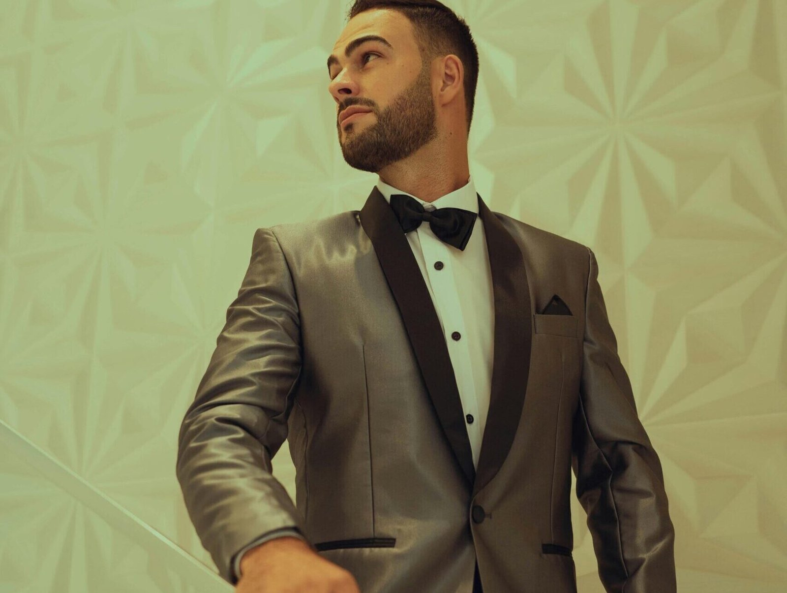 Portrait of a sophisticated man in a silver tuxedo standing indoors, exuding elegance.