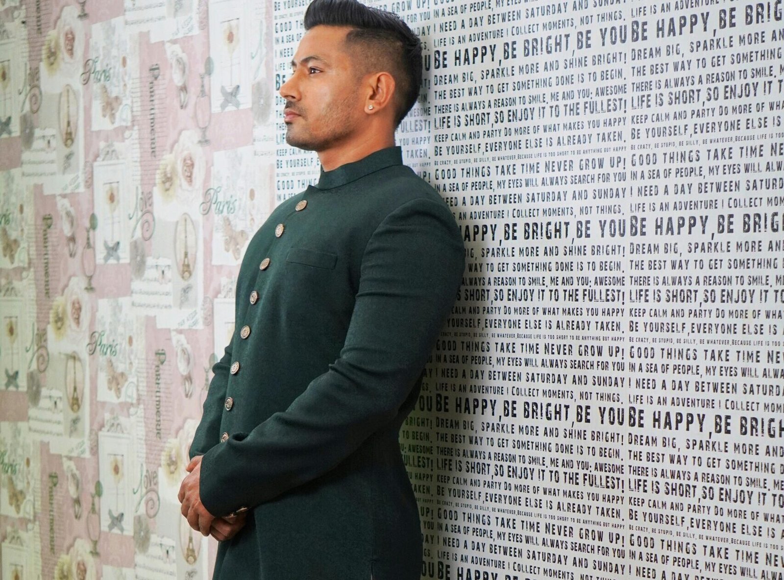 Side view of an Indian man in a green sherwani standing indoors with patterned walls.